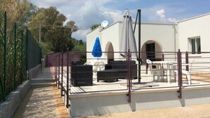 Une terrasse avec des sièges extérieurs, un espace couvert et un bâtiment blanc orné d’arcades.