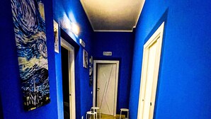 Un couloir aux murs bleus, avec un sol carrelé de carreaux jaunes, et une porte au fond.