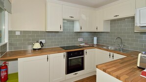 A compact kitchen with white cabinets, a built-in oven, a sink, and a wooden countertop. - The Bridge Suite, Invermoriston - The Great Glenway (Invermoriston)