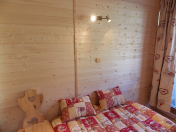 A wooden cabin interior with a bed, a wooden headboard, and a window with curtains.