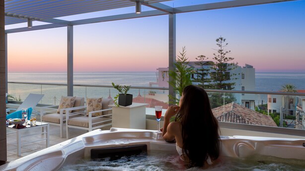 Une femme se détend dans un bain à remous, avec vue sur la mer et les bâtiments.