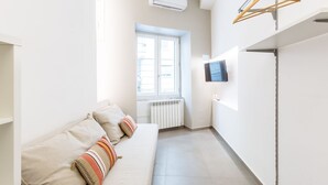 Una stanza moderna e luminosa con un divano, una TV a parete e una finestra con persiane.