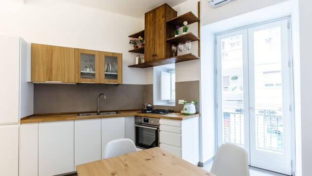 Una cucina moderna con mobili bianchi, un piano di lavoro in legno e un'area pranzo con tavolo e sedie in legno.
