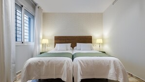 Ein Doppelzimmer mit zwei Betten, jeweils mit Holz Kopfteil, weißer Bettwäsche und je einer Nachttischlampe.