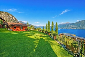 Una casa con techo rojo, un césped cuidado y vistas a un lago y montañas.