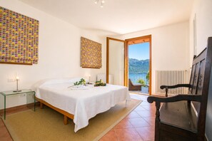A bedroom with a bed, bedside table, lamp, and a view of the outdoors. - Villa San Michele, Griante - Cadenabbia, Italy (Griante - Cadenabbia)