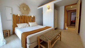 A bedroom with a bed, a bench, a wall-mounted lamp, and a door leading to another room.