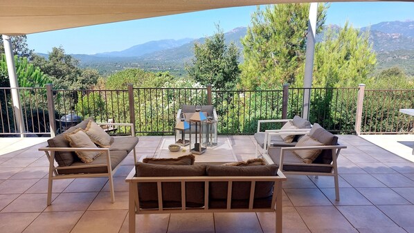 A terrace with outdoor furniture, a barbecue, and a view of mountains.