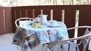 Un espace extérieur abrité, aménagé pour les repas, avec une table pour deux personnes, recouverte d’une nappe à motifs marins.