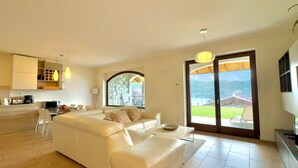 A spacious living area with a white sofa, a dining table, and a kitchen area with a built-in oven and microwave. - Villa Aurelia, Plesio, Italy (Plesio)