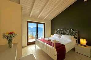 Ein Schlafzimmer mit Bett, Nachttisch, Lampe und Blick auf Berge durch eine Balkontür.