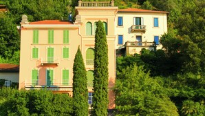 A multi-story building with a red roof, green shutters, and a balcony. It is surrounded by lush greenery and trees. - Villa Aurelia, Plesio, Italy (Plesio)