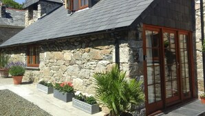 A stone building with a sloped roof, wooden windows, and a glass door.