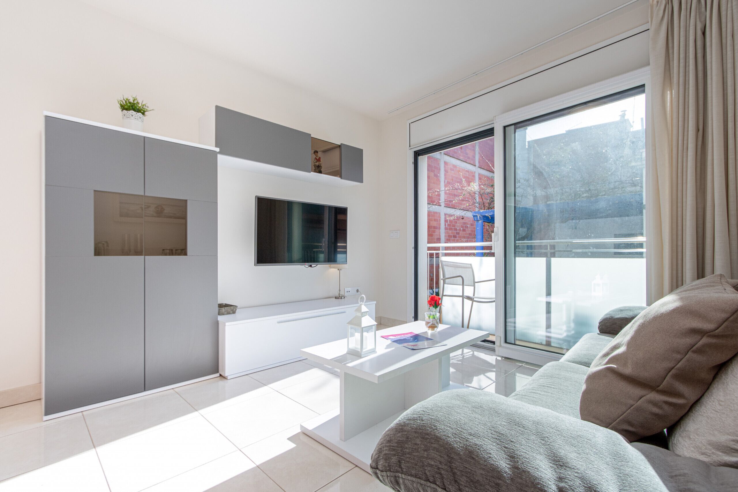 A modern living room with a flat-screen TV mounted on the wall, a white coffee table, and a grey sofa.