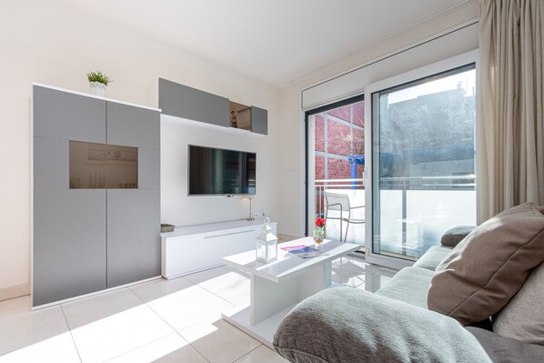Una sala de estar moderna con un televisor de pantalla plana montado en la pared, una mesa de centro blanca y un sofá gris.
