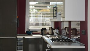 A modern kitchen with stainless steel appliances, a window with blinds, and a view of the outdoors. - Modern Villa with pool, sea view and mediterranean garden (Bari)