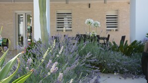 A garden with various plants and a cactus, a building with a brick facade, and a door. - Modern Villa with pool, sea view and mediterranean garden (Bari)