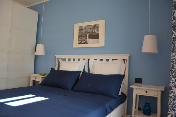 A bedroom with a bed, two bedside tables, a nightstand, a framed picture on the wall, and a blue curtain. - Apulia- Villa with pool with sea view. A perfect location to Puglia itineraries (Bari)