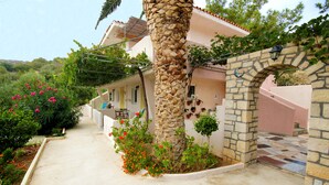 Una casa con un arco de piedra, una palmera y un jardín con flores rosadas.