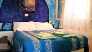 Un dormitorio con cama, almohadas, mesita de noche, lámpara y un cuadro en la pared.