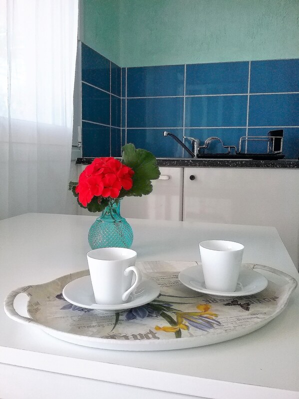 Una cocina con azulejos azules, una encimera blanca, un fregadero y una bandeja con dos tazas blancas y un jarrón con flores rojas.