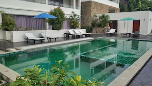 A swimming pool with lounge chairs and umbrellas, surrounded by a stone wall and greenery. - Tranquil Residence 1 (Koh Samui)