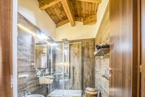 Moderni kylpyhuone, jossa on lasiseinällä varustettu suihku, peilillä varustettu pesuallas ja wc.