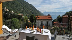 Ein Esstisch mit Blick auf die Berge, ein Balkon mit Stühlen und ein Gebäude mit rotem Dach.