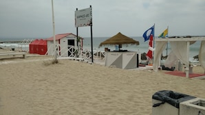 Ein Strand mit einer strohgedeckten Struktur, einem roten Zelt und einem Schild für Espaço 20 Black Bar.