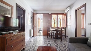 A living room with a TV, wooden dresser, patterned floor, and a dining area with chairs and a table.