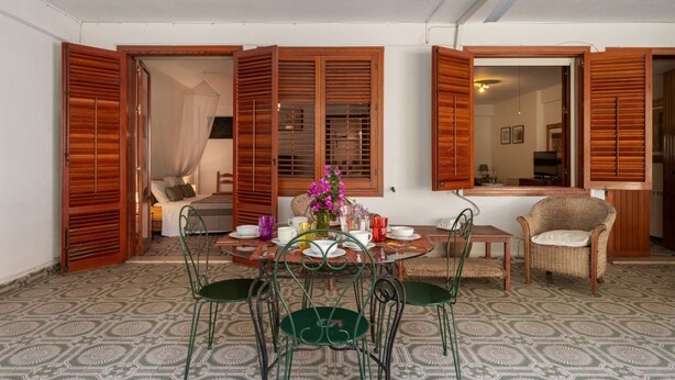 A dining area with a round table, green chairs, and a wicker chair. A bed with a canopy is visible in the background.