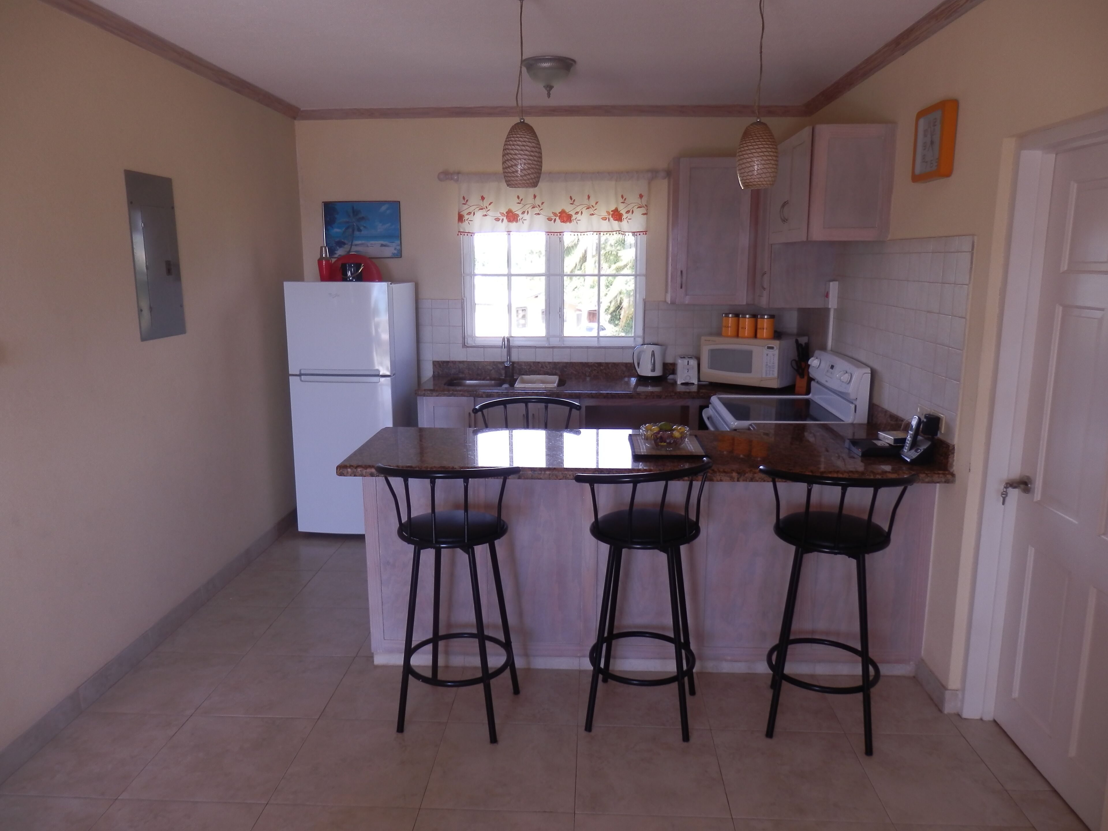 A kitchen with a central island, bar stools, a refrigerator, a microwave, and a sink.