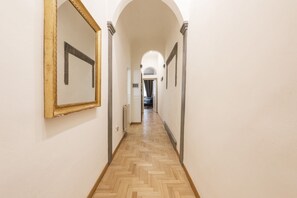 Un couloir avec un parquet en point de Hongrie, des murs blancs et un grand miroir sur le côté gauche.
