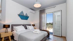 Ein Schlafzimmer mit einem Bett, zwei Nachttischen, einer Wandklimaanlage, einer Deckenleuchte und Blick durch eine Glasschiebetür.