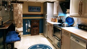 Une cuisine compacte équipée d’un four encastré, d’un four à micro-ondes et d’un lave-vaisselle. Un tapis bleu orné d’un motif en forme de boussole recouvre le sol.