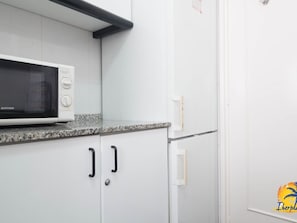 Compact kitchen with a microwave, refrigerator, and white cabinetry.