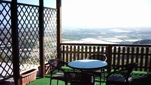 Ein überdachter Außenbereich mit Tisch und Stühlen, mit Blick auf eine Landschaft aus Feldern und einem fernen Horizont.