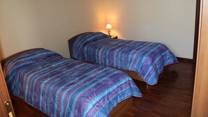 Ein Zimmer mit zwei Betten, jeweils mit einem gestreiften Überwurf, einem Nachttisch mit Lampe und Holzboden.