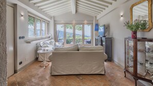 Een ruime kamer met een hoge plafond, een bank, een klein tafeltje en een kast met glazen deuren.