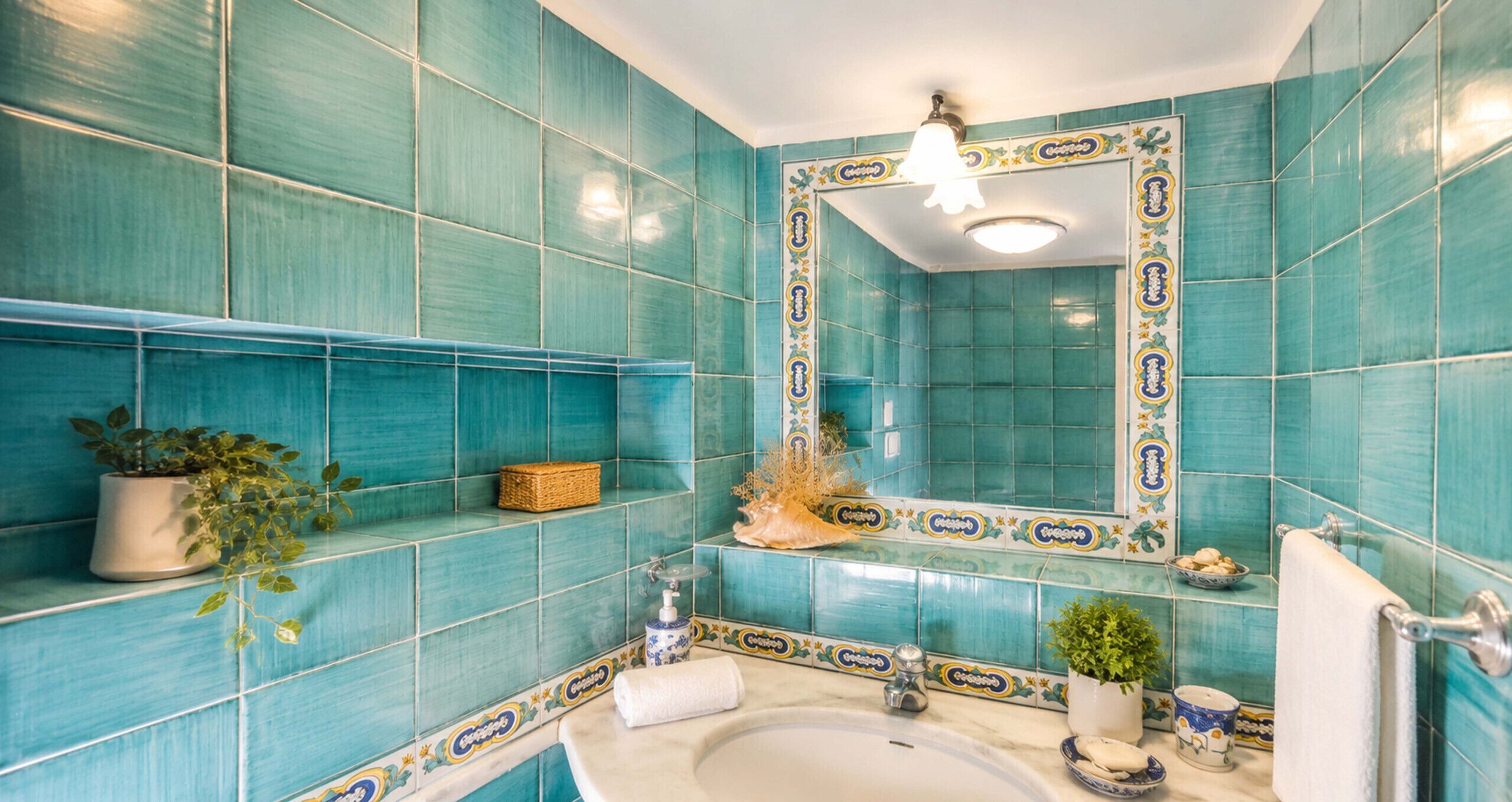 A bathroom with turquoise tiles, a white sink, a mirror with decorative frame, and a towel rack.