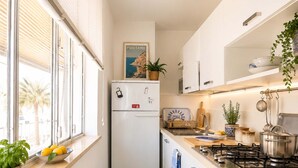 A narrow kitchen with a refrigerator, stove, and window with blinds. - AMORE RENTALS - Casa Raffi with Sea View on Positano’s Spiaggia Grande (Positano)