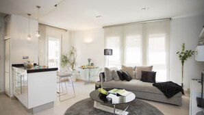 A modern living room with a grey sofa, a coffee table, and a kitchen area with a bar. - Singular Stays Poeta Querol (València)