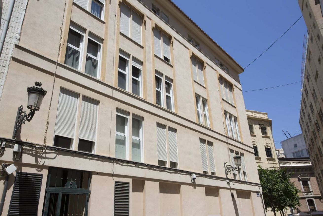 A multi-story building with a beige facade, multiple windows with shutters, and a street lamp on the corner.