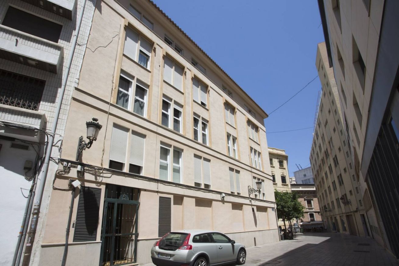A building with a beige facade, multiple windows, and a parked car in front.