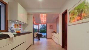 Eine moderne Küche mit weißen Schränken, ein Essbereich mit Tisch und Stühlen sowie ein Blick ins Freie.