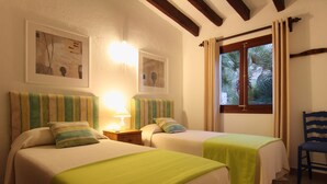 Ein Hotelzimmer mit zwei Betten, einem Sessel, einem Fenster mit Vorhängen und Bildern an den Wänden.