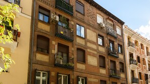 Un edificio de varios pisos con fachadas de ladrillo, varios balcones con plantas y una combinación de estilos de ventanas.