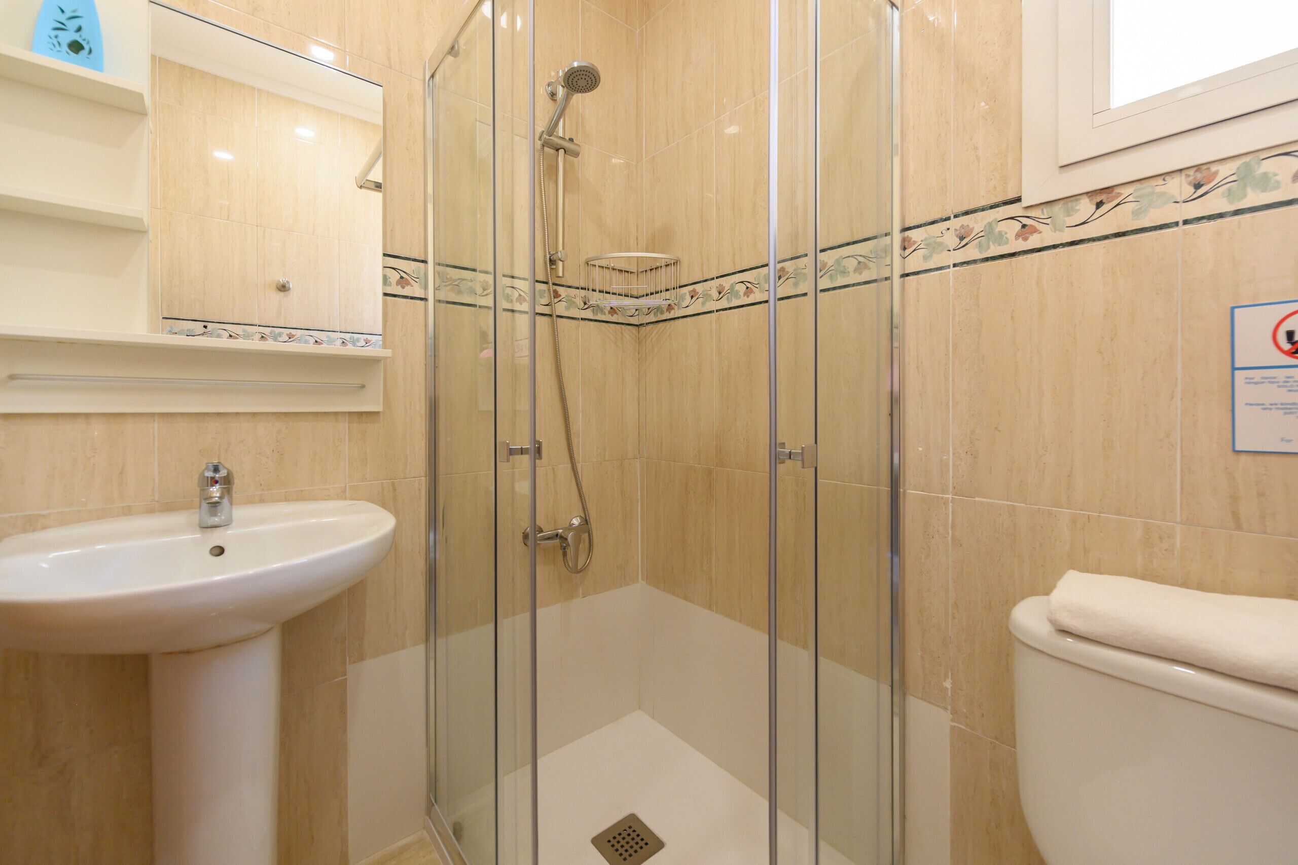 Un baño con ducha envuelta en vidrio, lavamanos y retrete.