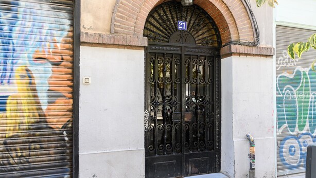 Una reja de hierro forjado negra con un letrero con el número 21 sobre ella, ubicada en un arco de ladrillo.