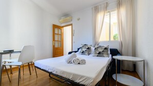 Una cama individual con colchón blanco, una mesita de noche, una silla y una ventana con cortinas.